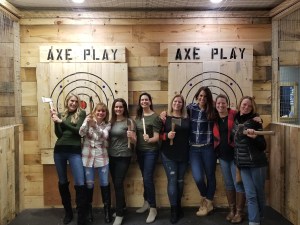Small group of women enjoying axe throwing at Axe Play in Hudson, NH, posing with axes in front of wooden targets.