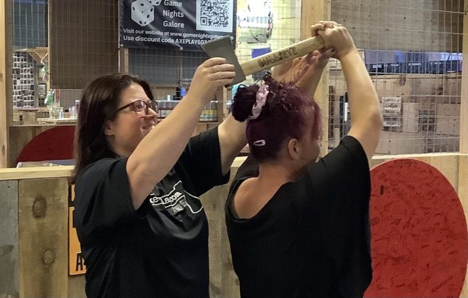 Axe throwing coach helping a beginner learn proper throwing technique at Axe Play