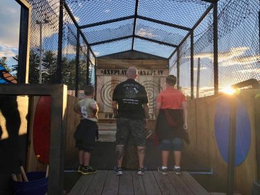 family learning how to throw an axe safely at Axe Play mobile trailer during sunset