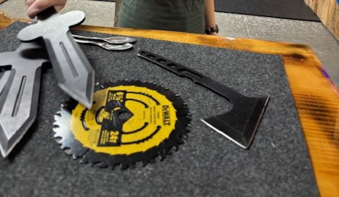 Fun Box axe throwing add-ons at Axe Play including throwing knives, saw blade, shovel, and spoons displayed on a lane table in Hudson NH.