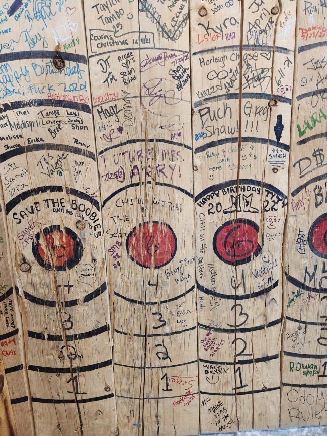 Axe throwing target wall covered in signatures from date nights and celebrations near Nashua NH
