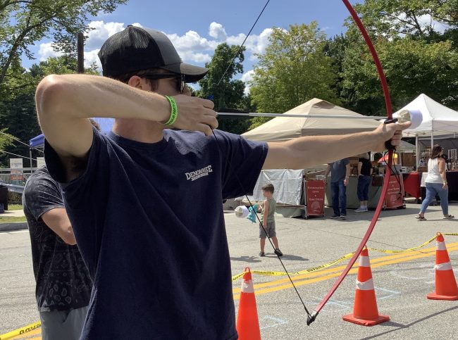 Guest using archery at a backyard party event with Axe Play mobile entertainment in New Hampshire