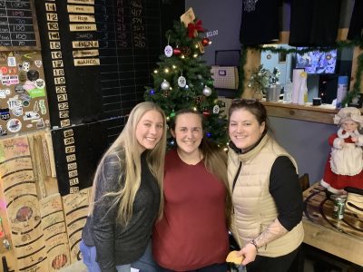 Three coworkers smiling beside Christmas decorations during a holiday party at Axe Play.